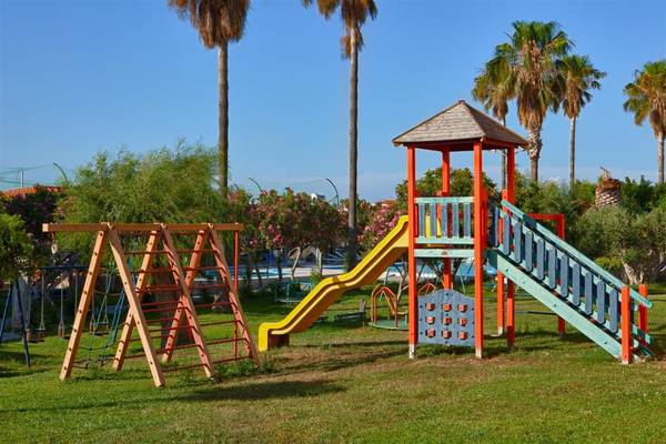 Spielplatz im Ilios K. Village Resort mit Rutsche, Klettergerüst und Pool im Hintergrund