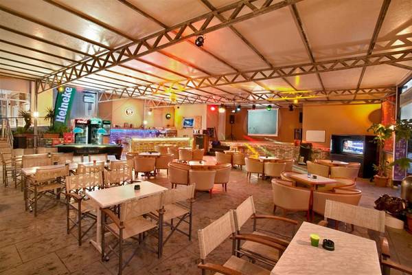 Lounge-Bereich des Ilios K. Village Resorts mit vielen Tischen und Stühlen, Bar und Fernseher.