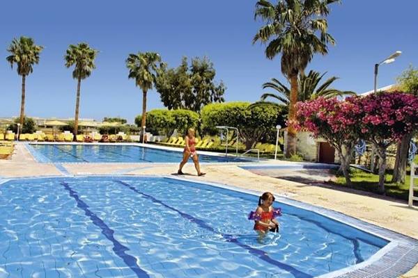 Außenpools im Ilios K. Village Resort mit Sonnenliegen und Bäumen.