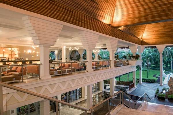 Innenansicht des Grand Riviera Princess Hotels mit mehreren Ebenen, Holzdecken, und einem Blick auf die Außenlandschaft.