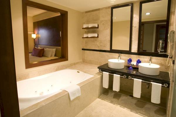 Badezimmer im Grand Riviera Princess Hotel mit Badewanne, Waschbecken und Spiegeln.