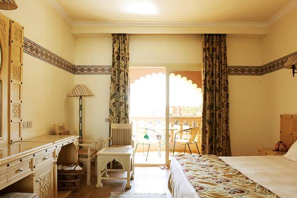 Ein Hotelzimmer im Sentido Mamlouk Palace mit einem Bett, Schreibtisch, Stühlen und einem Balkon.