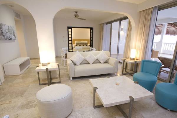 Wohnbereich des Grand Riviera Princess Hotels mit hellem Interieur, Couch, Tisch und Blick auf Schlafzimmer