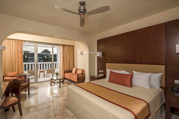 Innenansicht einer Suite im Grand Riviera Princess Hotel mit Bett, Wohnzimmer und Terrasse.