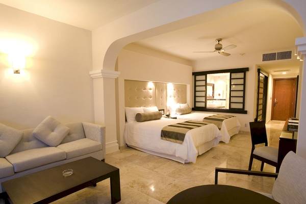 Suite-Schlafzimmer im Grand Riviera Princess Hotel mit zwei Betten, Sofa, Tisch und Deckenventilator.