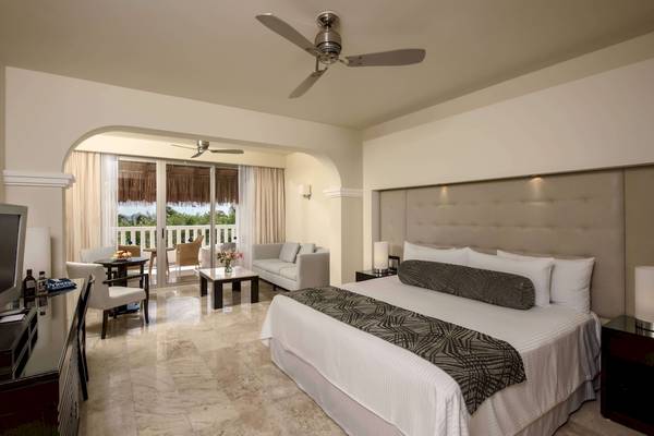 Schlafzimmer im Grand Riviera Princess Hotel mit Bett, Sofa und Balkonzugang.