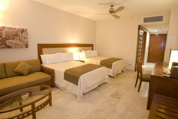 Doppelzimmer im Grand Riviera Princess Hotel mit zwei Betten, Sofa, Tisch und Deckenventilator.