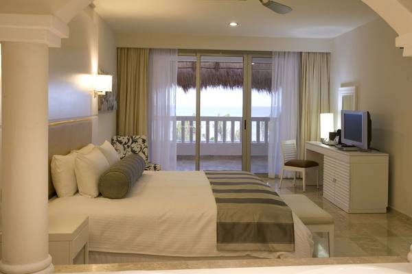 Innenansicht eines Schlafzimmers im Grand Riviera Princess Hotel mit Bett, Fenstern und Meerblick.
