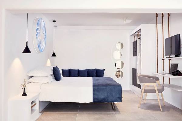 Schlafzimmer im Absolute Mykonos Suites & More Hotel mit weißem Bett, blauen Kissen, Dekoartikeln und einem Fernseher.