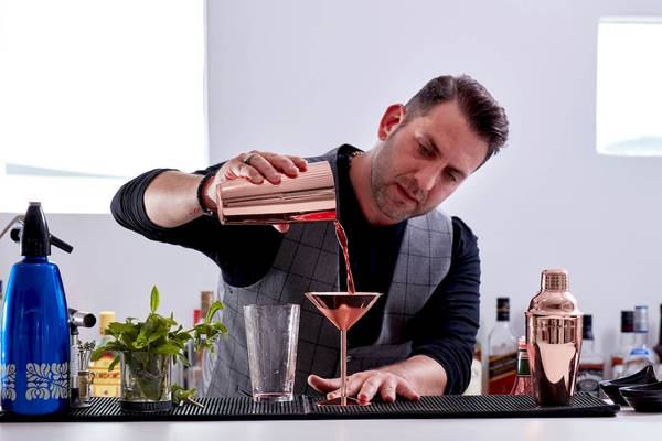 Ein Mann, der ein Glas mit einer silbernen Cocktailmischung füllt, steht an einer Bar.