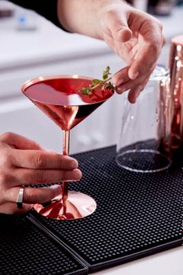 Barkeeper gibt einen Cocktail mit Thymian einhändig in ein Glas.