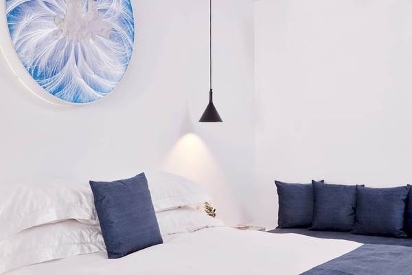 Schlafzimmer im Absolute Mykonos Suites & More mit weißem Bett, blauen Kissen und blauem Wandbild.