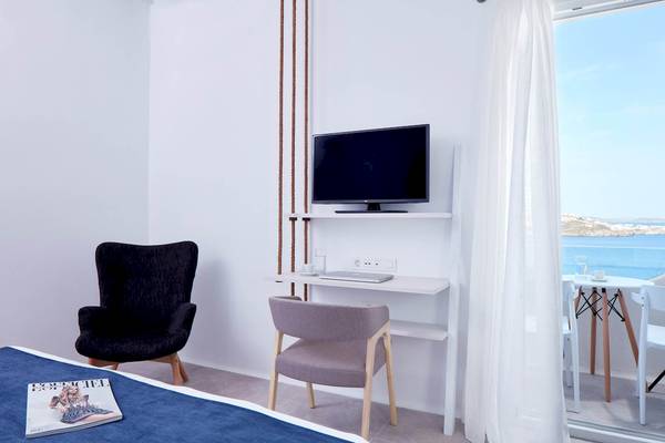 Innenansicht eines Zimmers im Absolute Mykonos Suites & More mit einem Schreibtisch, einem Fernseher und einem Bett.
