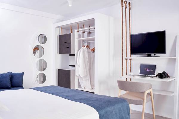 Innenansicht des Schlafzimmers im Absolute Mykonos Suites & More Hotel mit weißem Bett, Kleiderschrank und Schreibtisch.