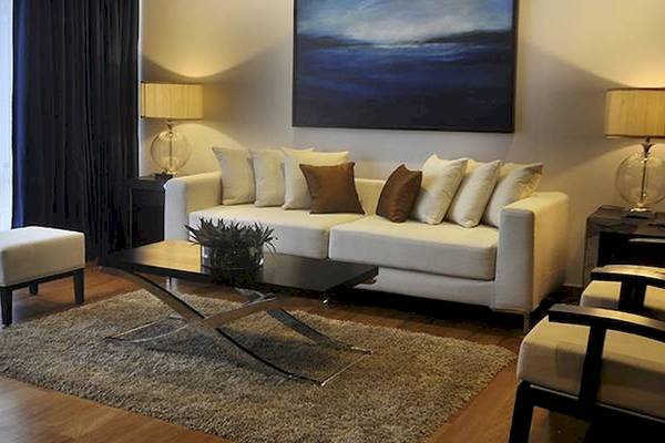 Wohnzimmer mit weißem Sofa, Beistelltischen mit Lampen und Teppich auf Holzboden.