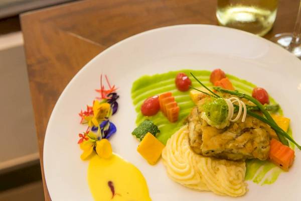 Ein Gericht auf einem weißen Teller, bestehend aus Fisch, Kartoffelpüree und Gemüse, mit einer grünen Sauce und dekorativen Blumen.