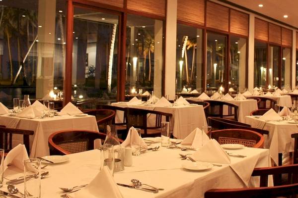 Ein elegantes Restaurant im Blue Water Hotel und Spa mit gedeckten Tischen und Stühlen, großen Fenstern und Blick auf die Außenbeleuchtung.