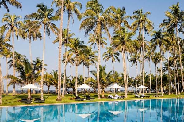 Der Poolbereich des Blue Water Hotel and Spa mit vielen Palmen und Sonnenschirmen.