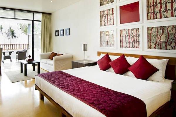 Ein Zimmer im Blue Water Hotel and Spa mit einem großen Bett, roten Kissen und einer Aussicht auf eine Terrasse.