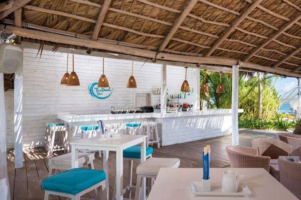 Strandbar des Catalonia Royal Bavaro Hotels mit weißen Tischen, blauen Stühlen und Blick auf das Meer.