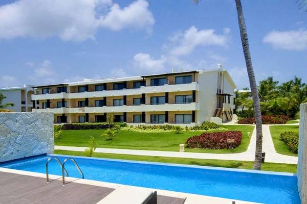Außenansicht des Catalonia Royal Bavaro Hotels mit Swimmingpool und grüner Rasenfläche.