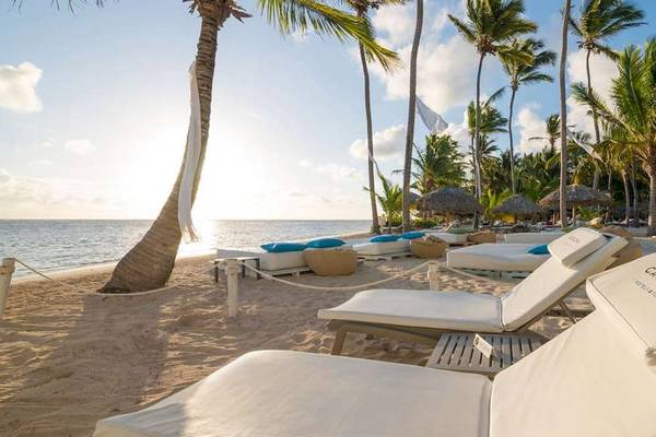 Sonnenaufgang am Strand des Catalonia Royal Bavaro mit weißen Liegen, Palmen und blauem Himmel.