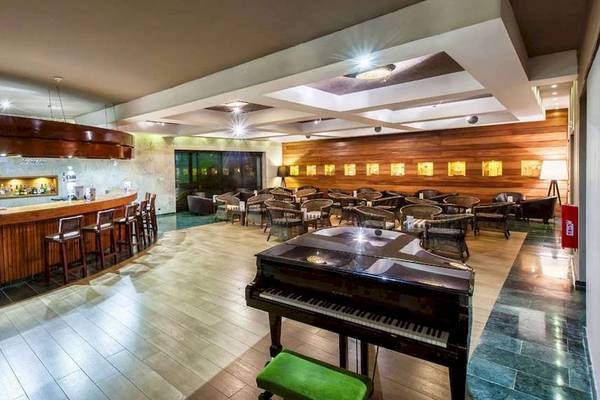 Innenbereich des Hotels Catalonia Royal Bavaro mit Bar, Klavier und runden Tischen.