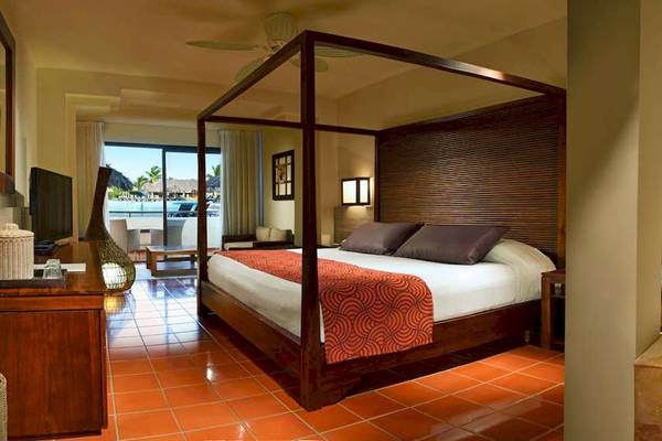 Innenansicht eines Hotelzimmers im Catalonia Royal Bavaro mit einem Himmelbett, einem Fernseher und einem Ausblick auf den Pool.