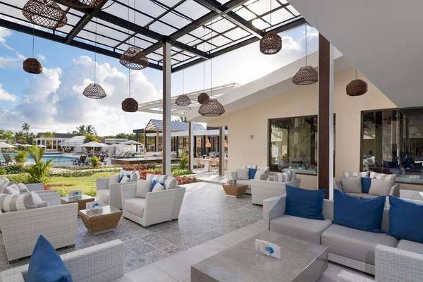 Loungebereich im Catalonia Royal Bavaro Hotel mit weißen Möbeln, blauen Kissen und einer Aussicht auf einen Pool.