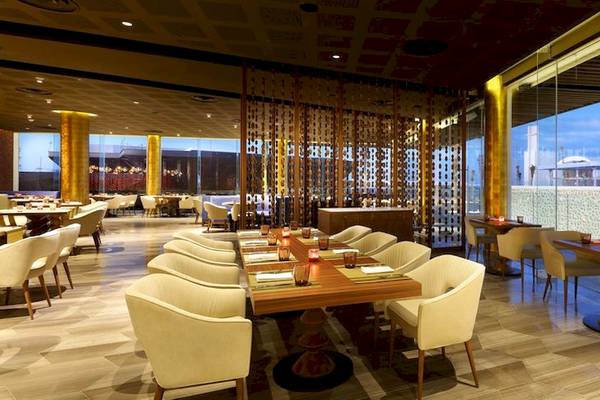 Innenansicht des Restaurants im Grand Palladium Costa Mujeres Resort mit runden Tischen, weißen Stühlen und großen Fenstern.