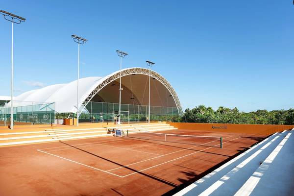Tennisanlage im Grand Palladium Costa Mujeres Resort & Spa mit blauem Himmel und orangefarbenen Wänden.