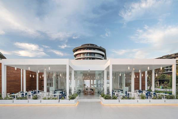 Außenbereich des Voyage Belek Golf & Spa Hotels mit modernem Design und vielen Tischen und Stühlen.