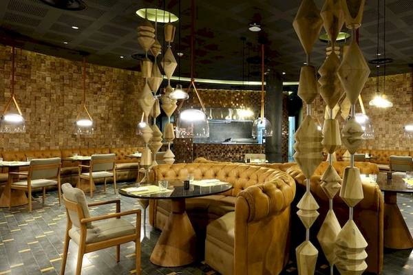 Innenbereich des Grand Palladium Costa Mujeres Resort & Spa mit geometrischen Pendelleuchten, braunen Ledersofas und runden Tischen.