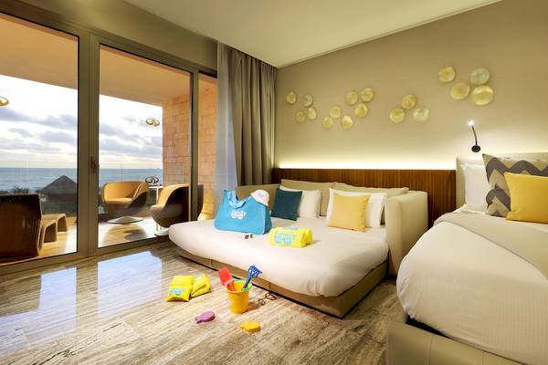 Zimmer im Grand Palladium Costa Mujeres Resort & Spa mit Meerblick, zwei Betten, Möbeln und Spielzeug.