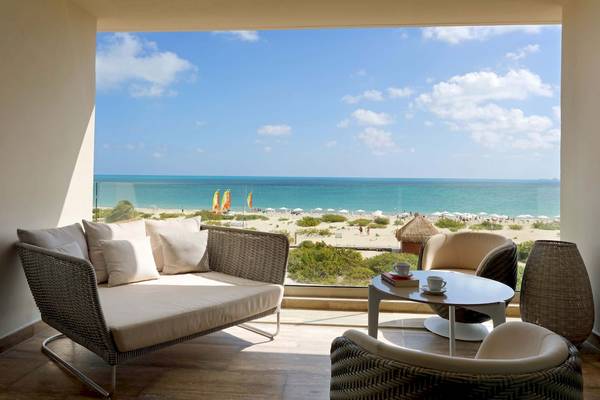 Blick aus einem Zimmer des Grand Palladium Costa Mujeres Resorts auf das Meer mit Sonnenschirmen und Segelbooten.