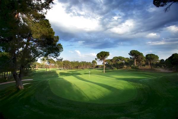 Golfplatz des Voyage Belek Golf & Spa mit Bäumen und einer Fahne im Schatten.