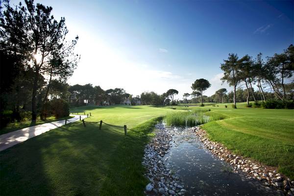 Golfplatz im Voyage Belek Golf & Spa mit grünen Rasenflächen und einem Bach.