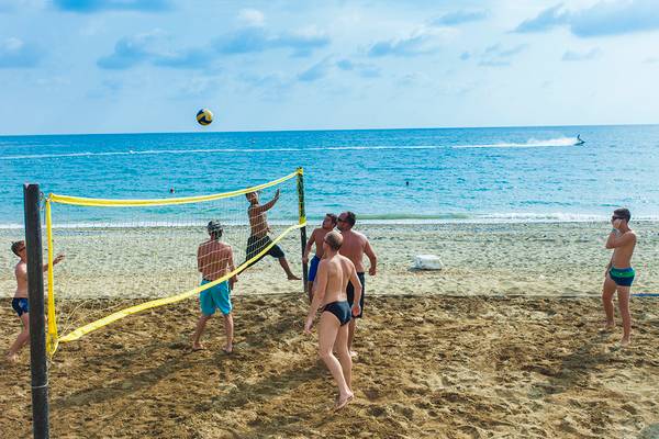 Gruppe von Männern spielt Volleyball am Strand mit Netz und Ozean im Hintergrund.