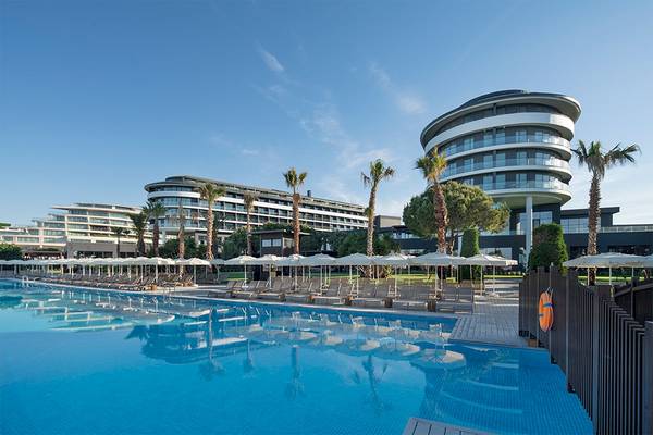 Außenbereich des Voyage Belek Golf & Spa Hotels mit Swimmingpool, Sonnenliegen und Palmen.