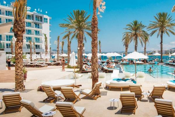 Strandlounge am Pool des Amare Beach Hotel Ibiza mit Liegestühlen, Sonnenschirmen und Palmen.