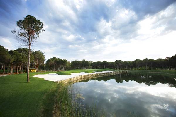 Golfplatzansicht des Voyage Belek Golf & Spa mit Wasserhindernis und Bäumen.