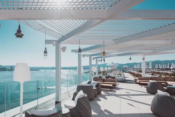 Terrasse des Amare Beach Hotel Ibiza mit Meerblick, Sonnenliegen, Lampen und blauem Himmel.