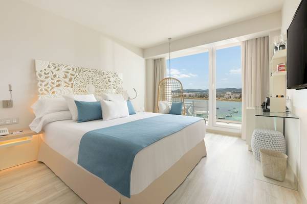 Zimmer im Amare Beach Hotel Ibiza mit Blick auf das Meer und weißem Bett.