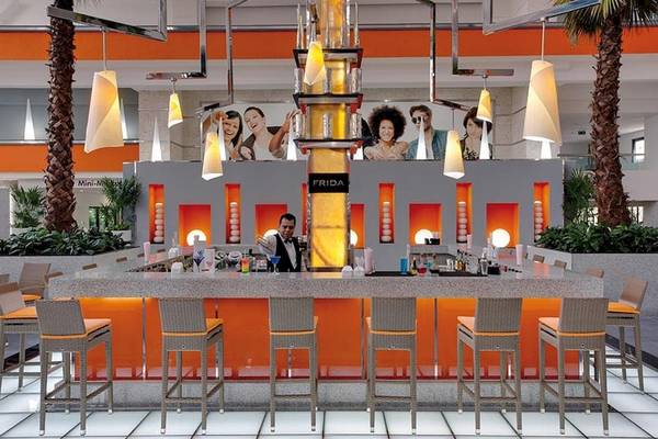 Frida Bar im Riu Caribe Hotel mit Barkeeper und orangefarbenen Stühlen.