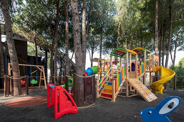 Spielplatz im Wald mit bunten Spielgeräten und einem gelben Rutschbecken im Voyage Belek Golf & Spa Hotel.