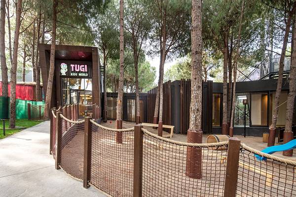 Eingangsbereich des Tugi Kids World im Voyage Belek Golf & Spa Hotel mit Bäumen und Spielgeräten.