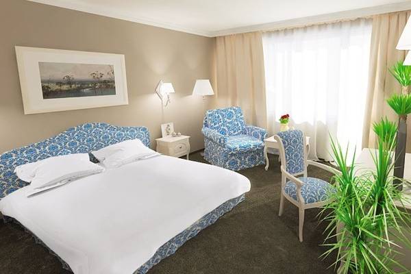 Schlafzimmer im Sofia Hotel mit Doppelbett, Stühlen, Nachttischen und Fenstern mit Vorhängen.