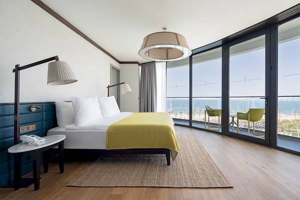 Voyage Belek Golf & Spa Hotelzimmer mit Aussicht auf das Meer, Bett, Lampen und Glastüren.