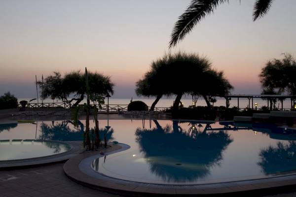 Abendstimmung am Pool im Baia del Sole Hotel mit reflektierten Bäumen und dem Meer im Hintergrund.