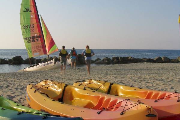 Segelboot am Strand von Baia del Sole mit drei Personen in Schwimmwesten und Kajaks auf dem Sand.
